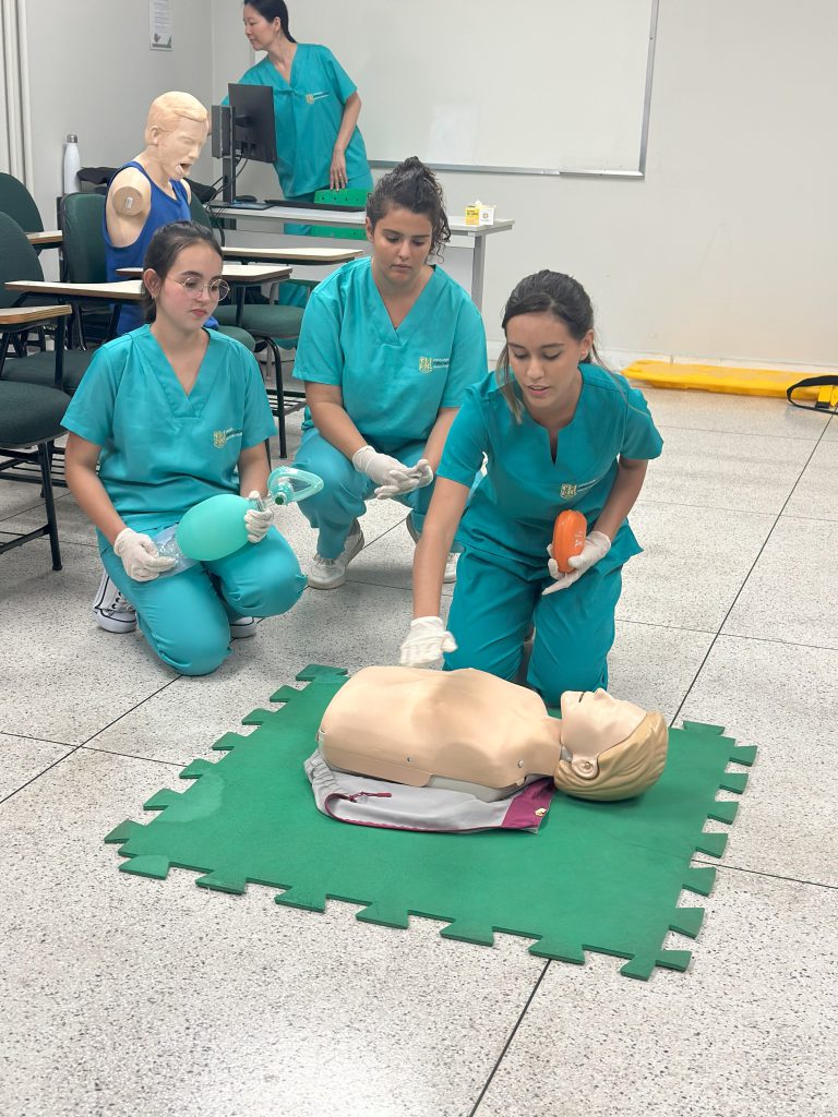 Alunas do curso de Enfermagem da FCM-MG realizam simulação de atendimento de urgência com manequim durante aula prática.
