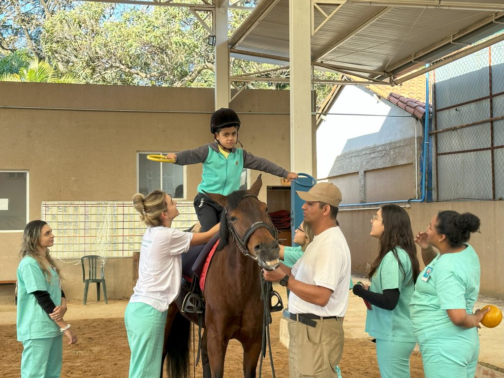 Aluno do curso de Fisioterapia da FCM-MG participa de aula prática de equoterapia, com o apoio de professores e colegas em ambiente supervisionado.